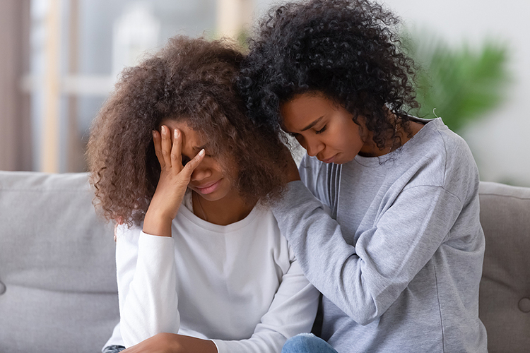 Image of an adult Black woman comforting a Black young adult girl.